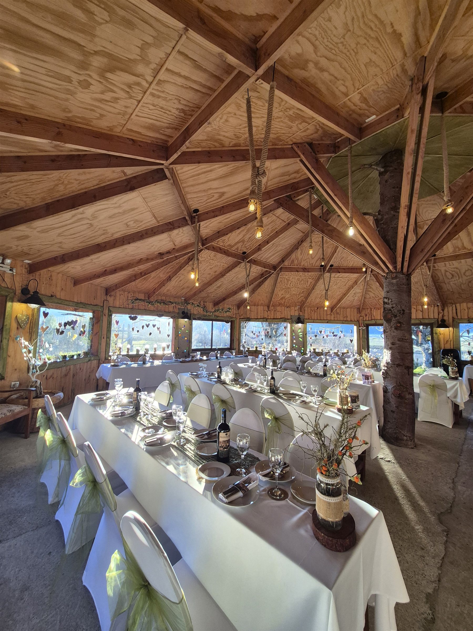 Mesas largas decoradas con manteles blancos y centros de flores silvestres bajo el techo de madera